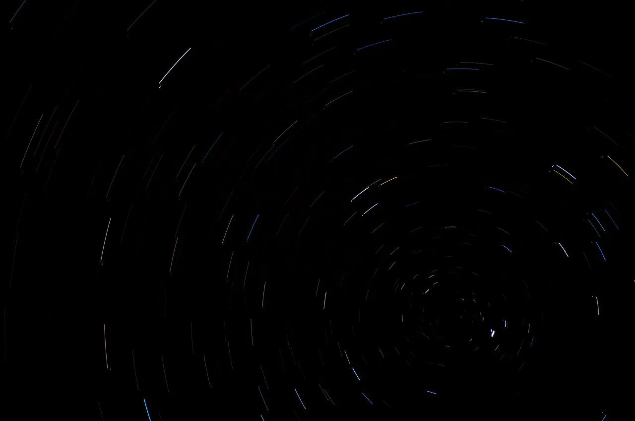 A long-exposure night photograph showing stars tracing concentric circular arcs around a nearly stationary point in the sky, Polaris.