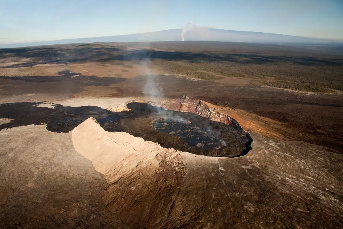 Looking up the gentle slope of Kilauea volcano in Hawaii, with fresh lava erupting from the Puu Oo vent in the foreground and an ash plume rising from the summit behind.
