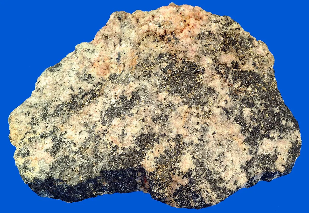 An ore specimen with metallic galena and brassy pyrite grains set in rock alongside pale quartz and feldspar.