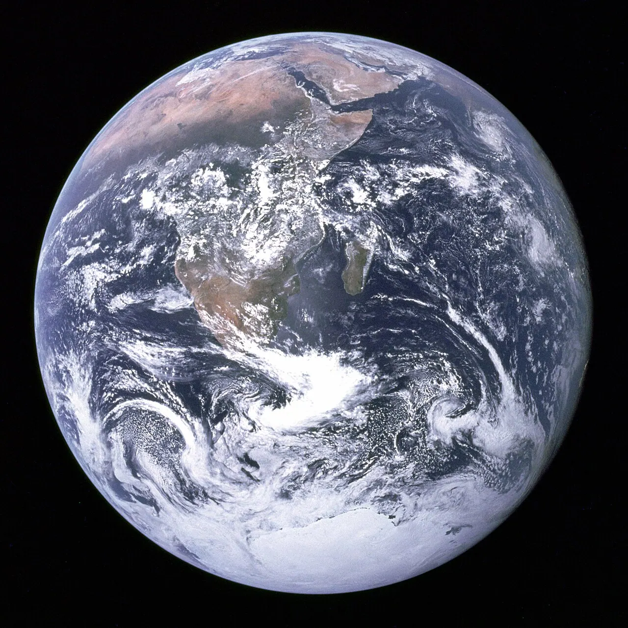 The Blue Marble: the full disk of Earth photographed from space, showing Africa, the Arabian Peninsula, Antarctica, and swirling white clouds over blue ocean.